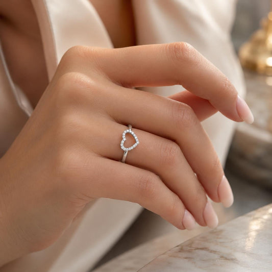 A close-up of a person's hand wearing a silver ring with a heart-shaped gemstone.