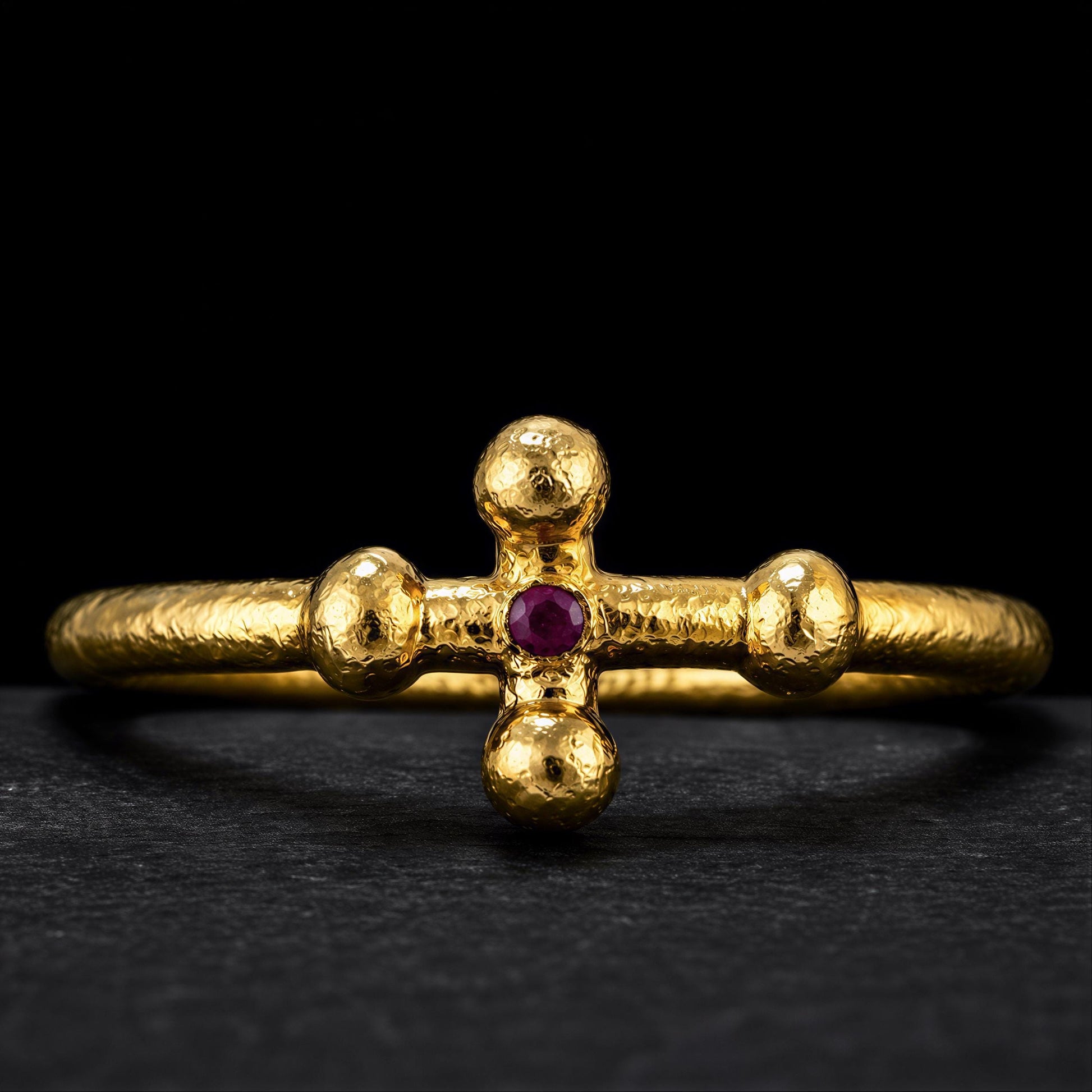 A gold ring with a cross-shaped gemstone in the center, set against a black background.