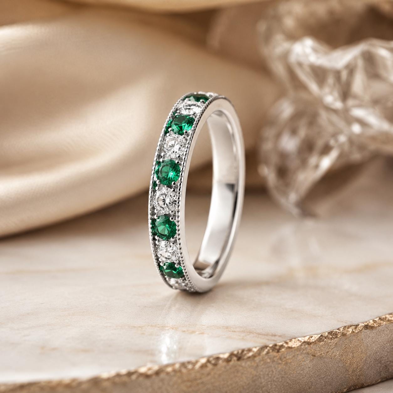 A silver ring with a band of green and white diamonds, set against a beige background.