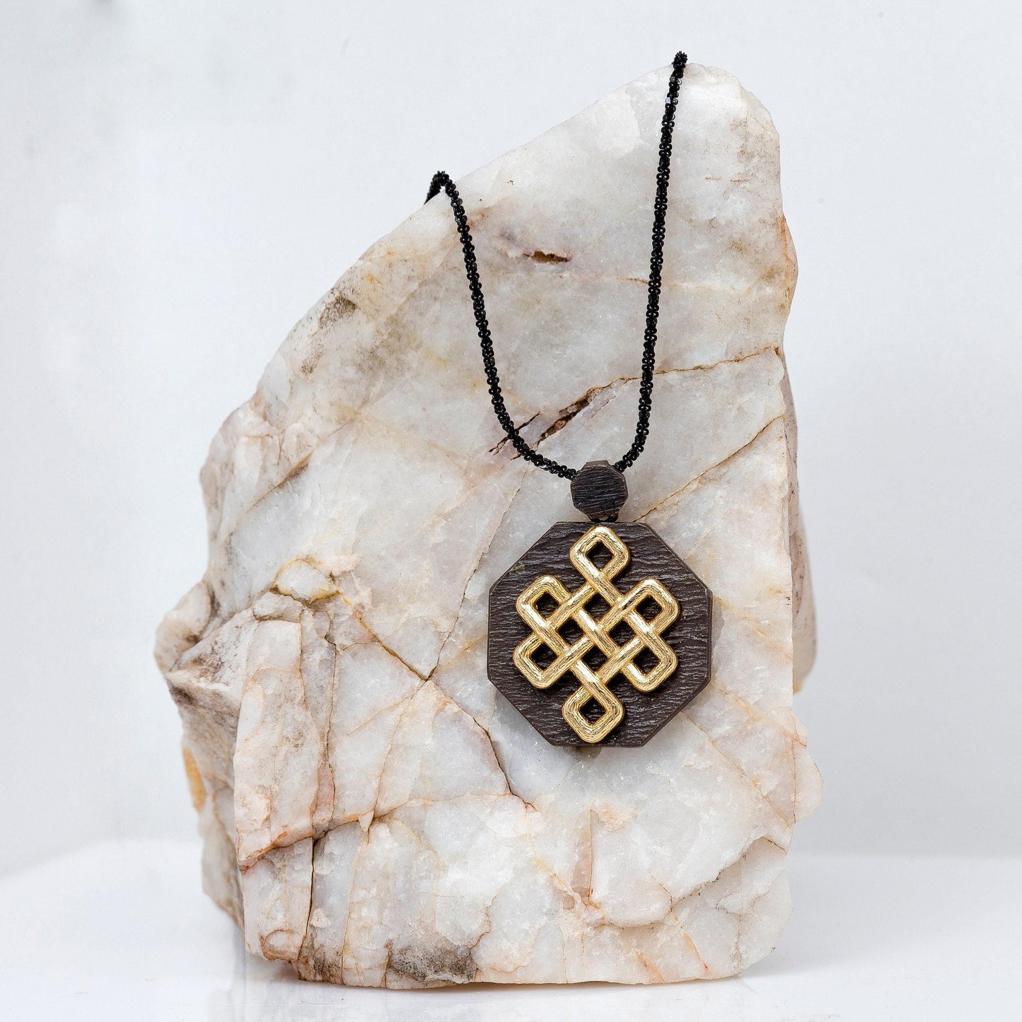 A necklace with a wooden pendant featuring a golden geometric design is displayed on a white marble surface.