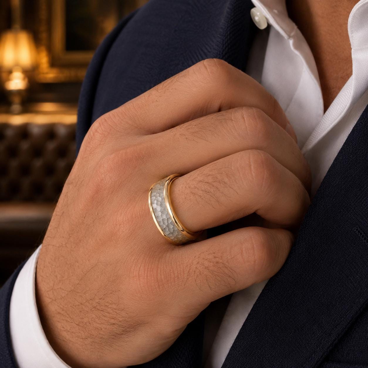 A close-up of a man's hand wearing a gold ring, with a blurred background that appears to be a room with a couch and a lamp.