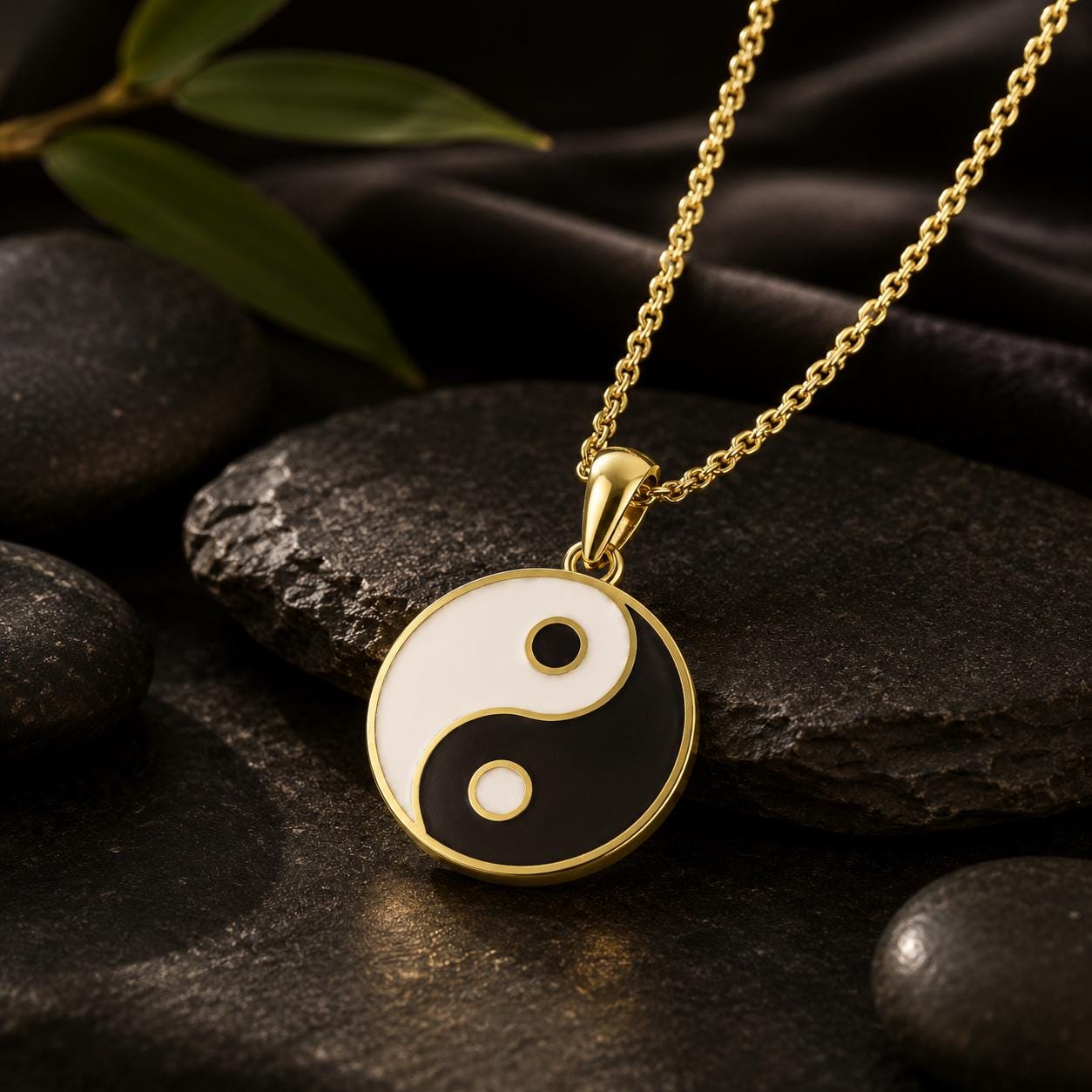 A gold-colored pendant necklace with a black and white yin and yang symbol pendant is displayed on a dark surface, surrounded by rocks.