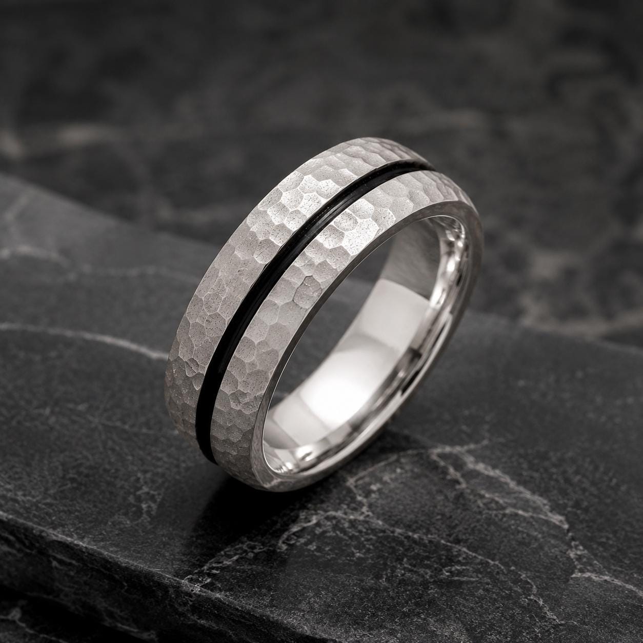 A silver ring with a black band is displayed on a dark surface.