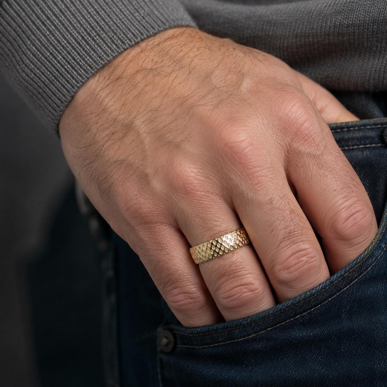 A close-up of a person's hand wearing a gold ring on the ring finger, with the hand resting in the pocket of a pair of blue jeans.