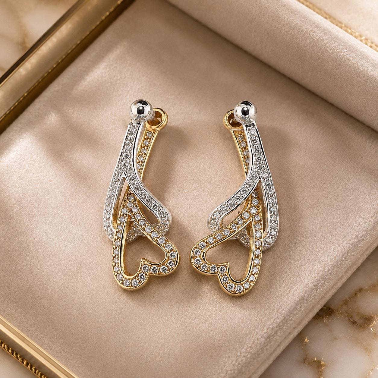 A pair of elegant gold and silver earrings with sparkling crystal accents, displayed on a beige velvet background.