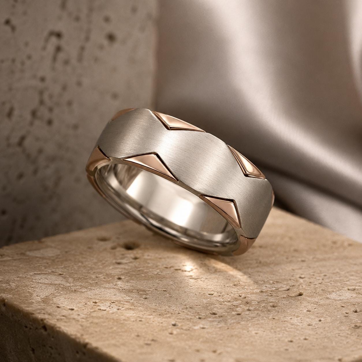 A silver ring with a geometric design sits on a textured surface.
