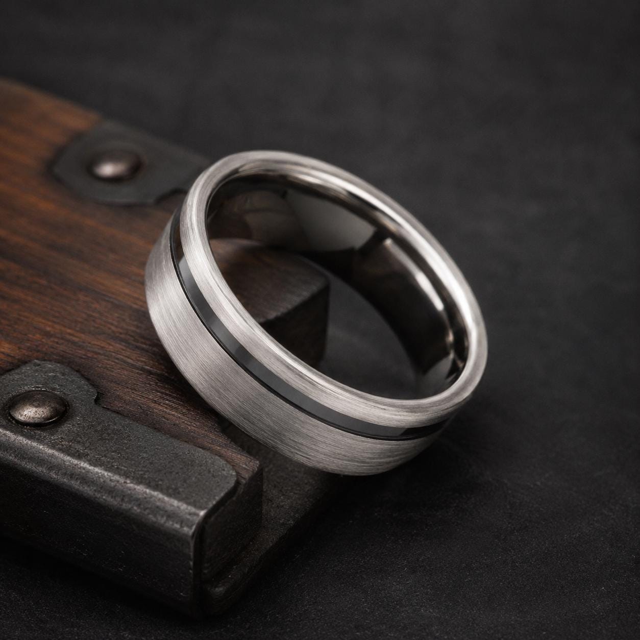 A silver ring with a black band is resting on a wooden surface.