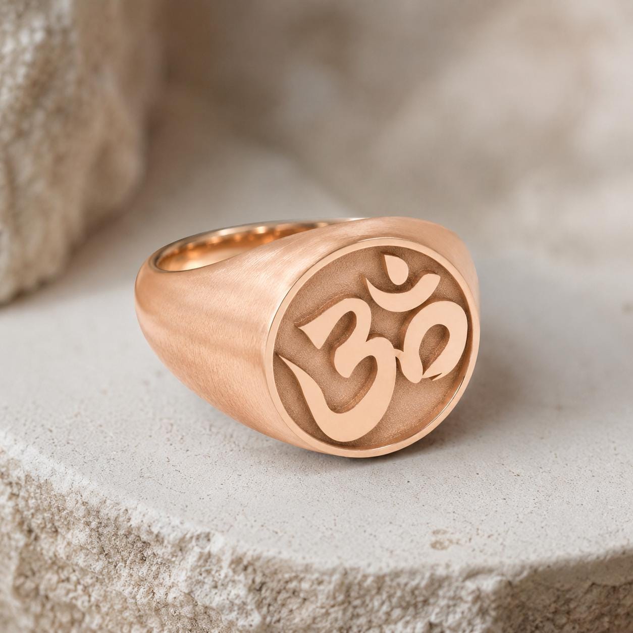 A gold-colored ring with the Om symbol engraved on it, resting on a stone surface.