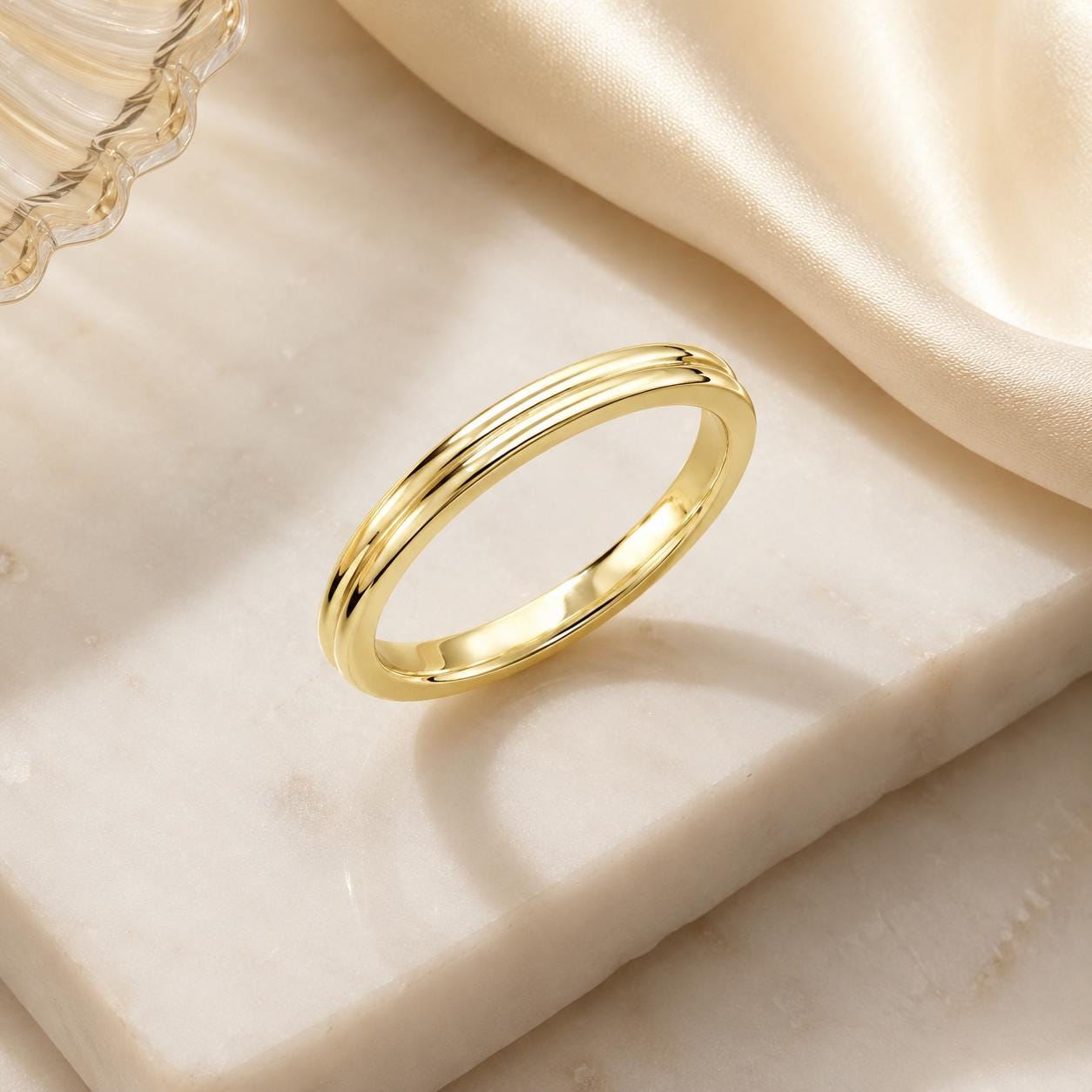 A gold ring is displayed on a white marble surface, casting a shadow.