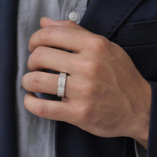 A close-up of a person's hand wearing a silver ring on the ring finger.