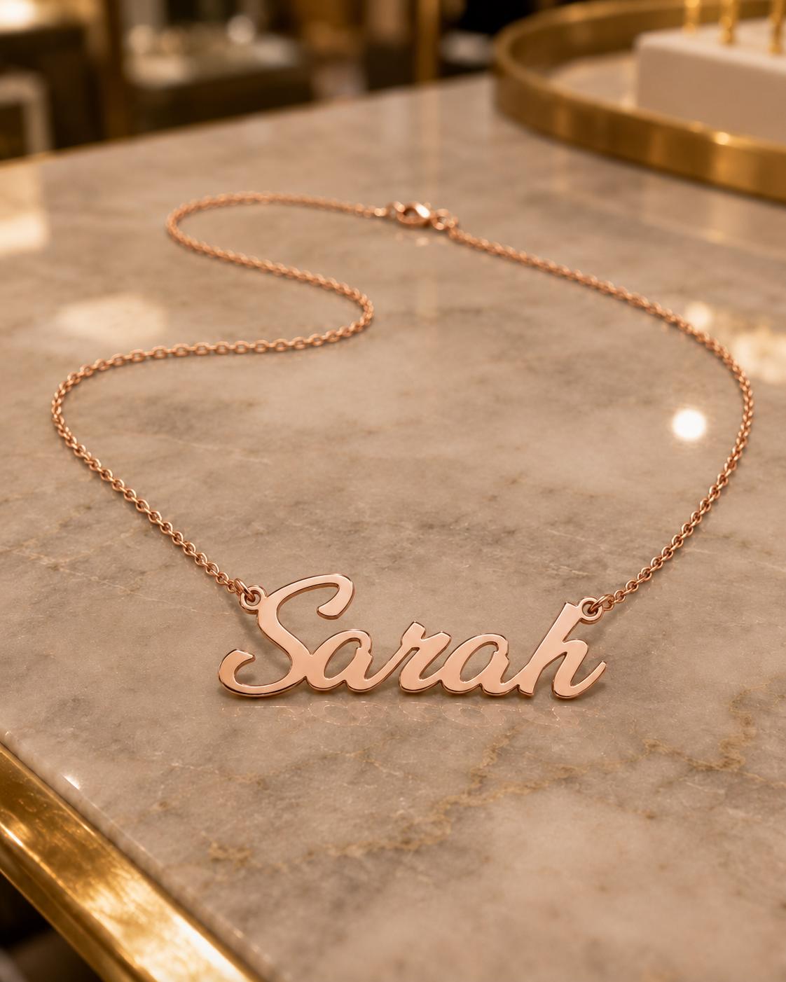 A necklace with the name "Sara" engraved on it, resting on a marble surface.