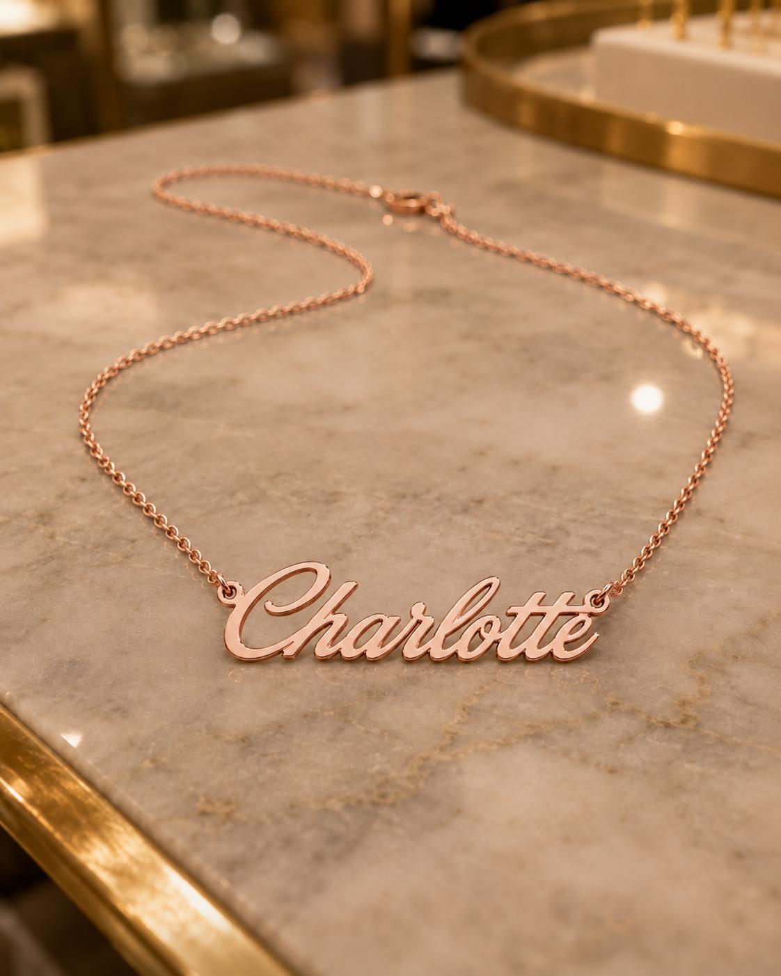 A necklace with the name "Charlotte" engraved on it, resting on a marble surface.