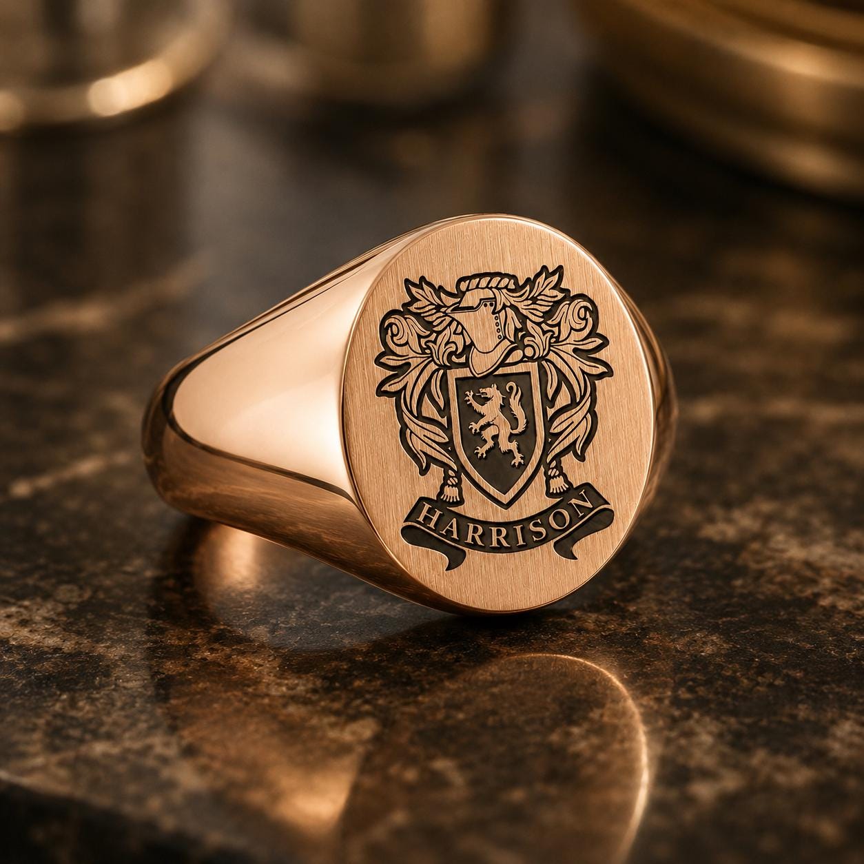 A gold-colored signet ring with a crest and the name "HARRISON" engraved on it, placed on a dark surface.