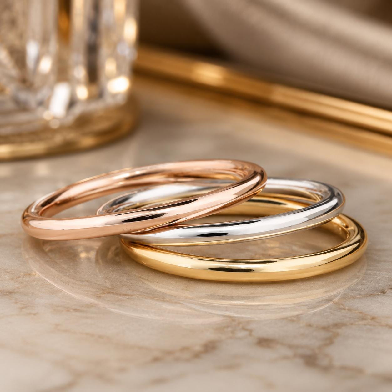 Three rings of different colors - gold, silver, and copper - are arranged on a marble surface.