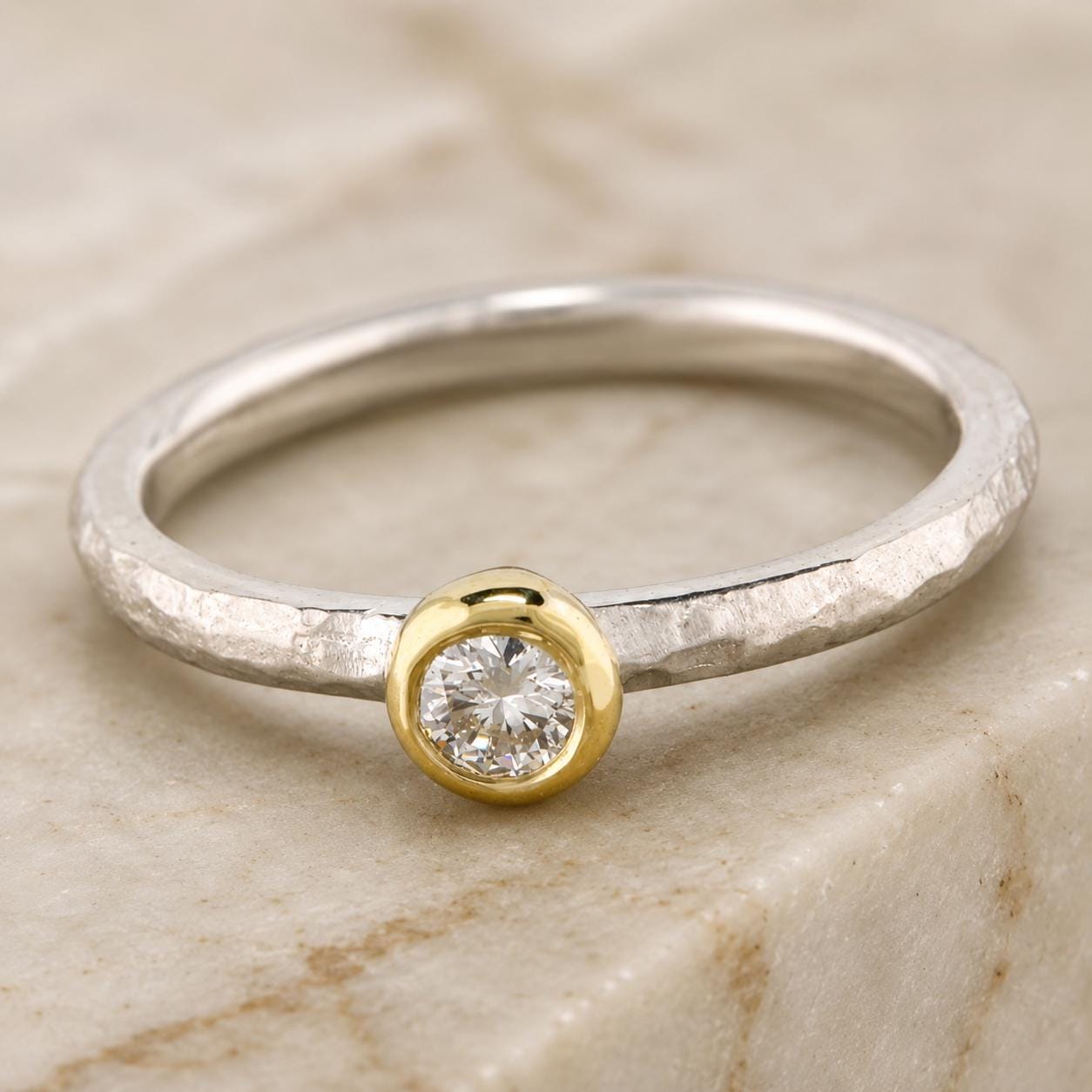 A silver ring with a large diamond set in the center, resting on a marble surface.