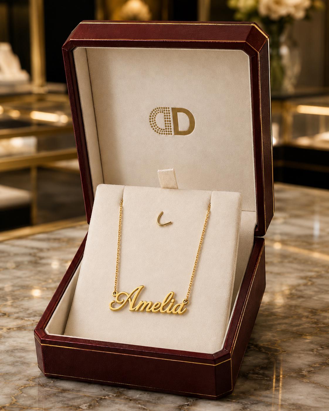 A gold necklace with the name "Amelia" engraved on it, displayed in a burgundy jewelry box.