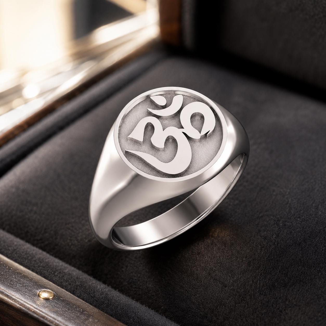 A silver ring with the Om symbol engraved on it, placed on a black surface.