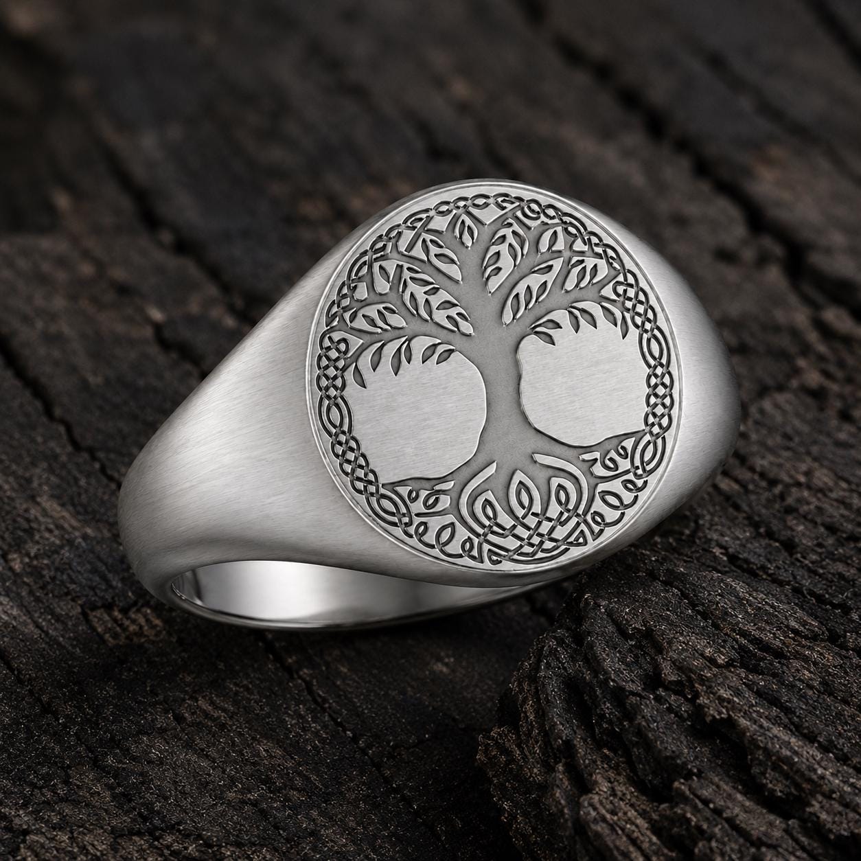 A silver ring with an intricate tree design on it, resting on a wooden surface.