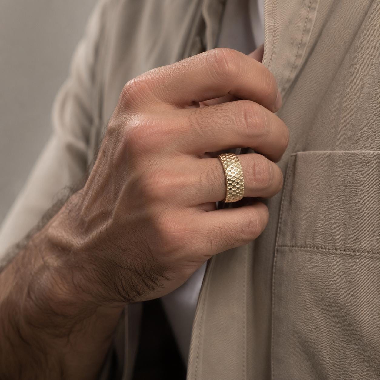 A close-up of a person's hand adjusting their tie, wearing a gold ring on their finger.