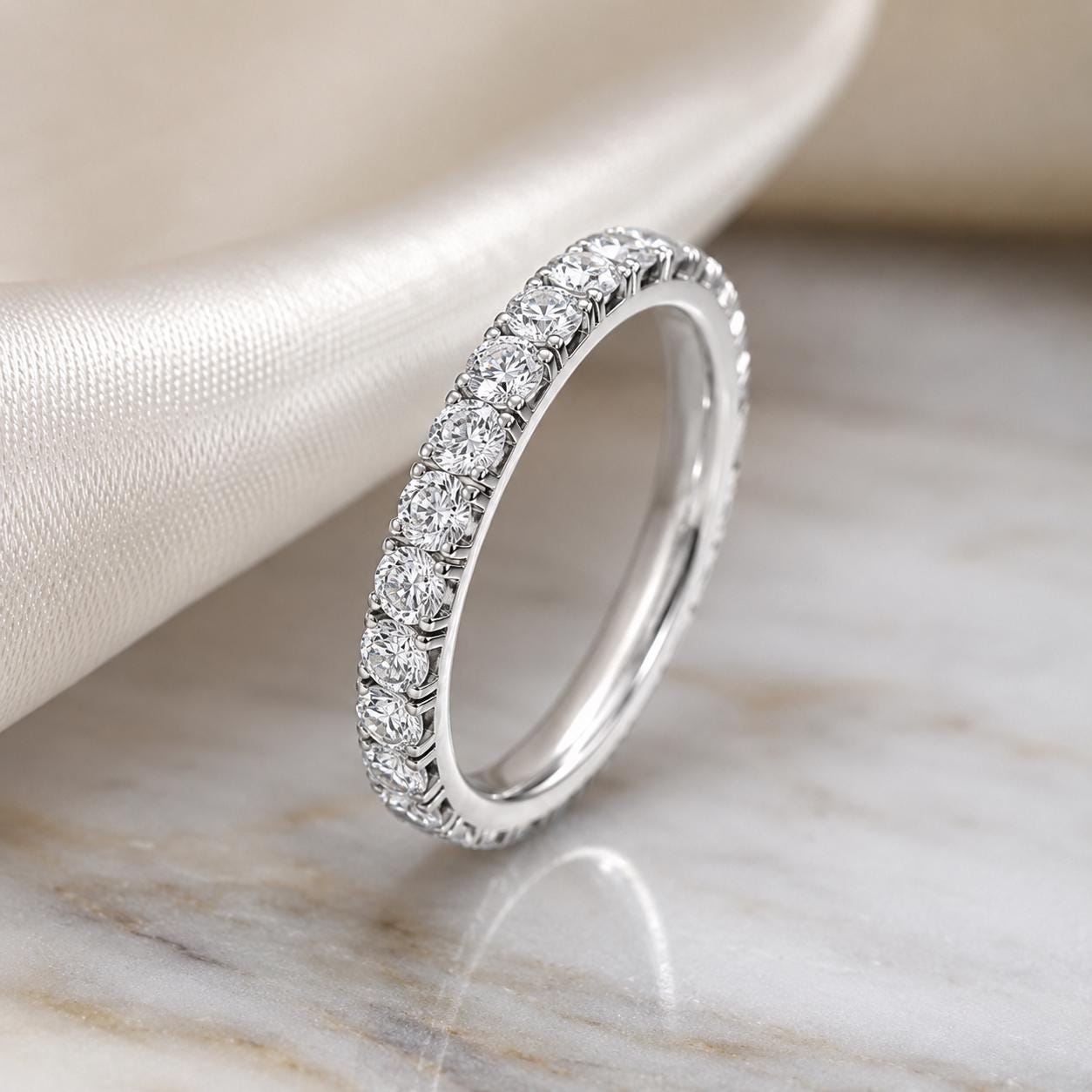 A diamond-encrusted ring with a row of diamonds set in a band, resting on a marble surface.