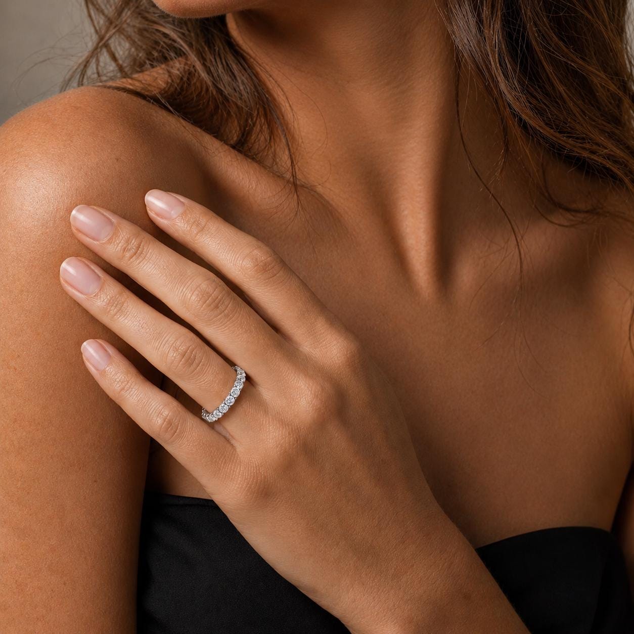A close-up of a woman's hand wearing a diamond ring on her finger, with her shoulder and neck visible.