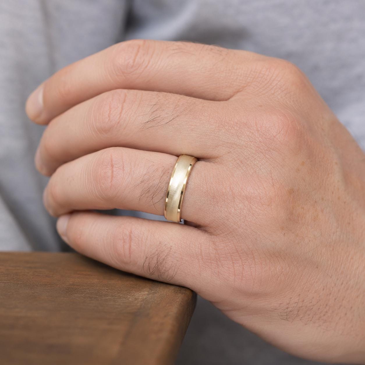 A close-up of a person's hand wearing a gold wedding ring.