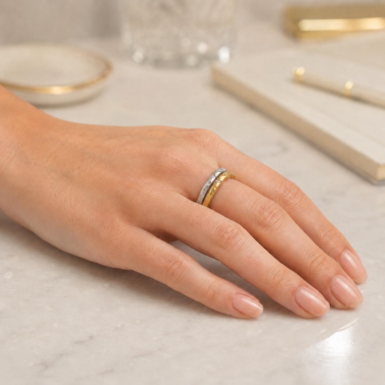 A close-up view of a person's hand wearing a ring on the ring finger, with a marble surface in the background.