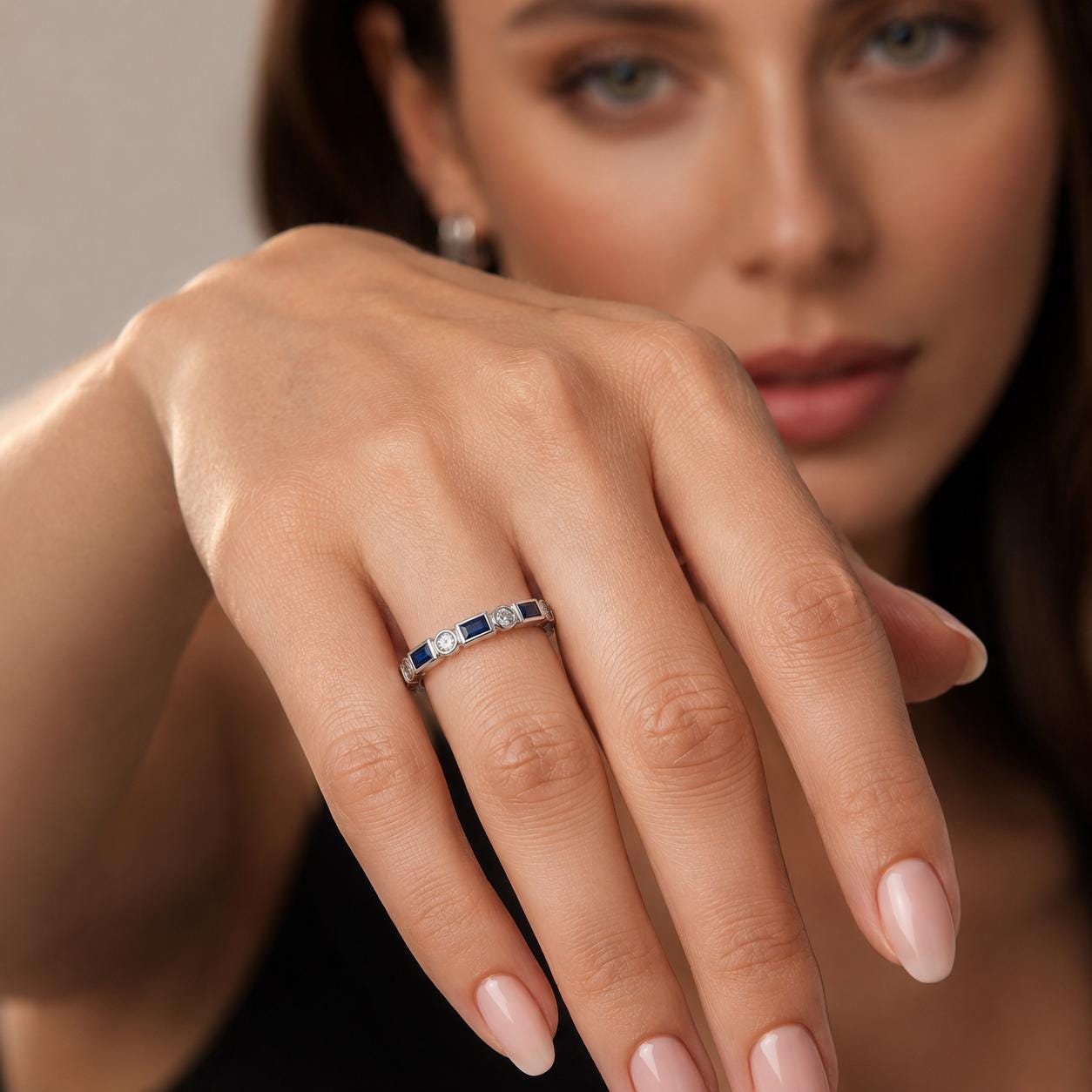 A close-up of a woman's hand wearing a ring with blue and white stones.