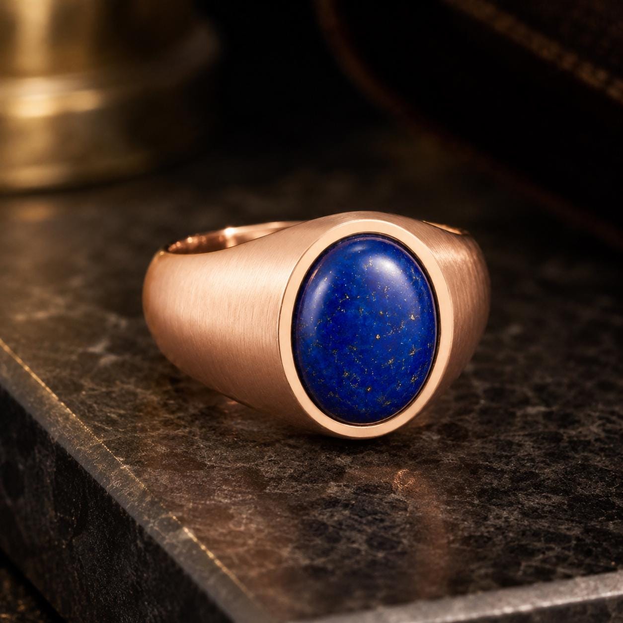 A gold ring with a blue lapis lazuli stone set in the center, resting on a dark surface.