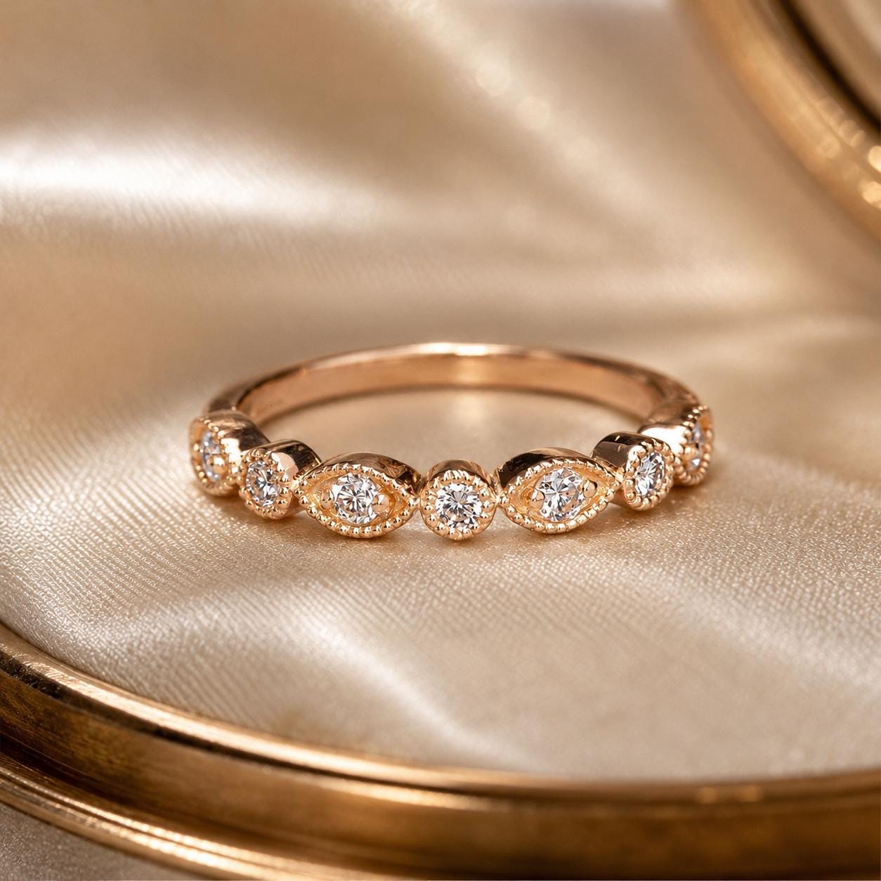 A gold ring with a row of small diamonds set in the center, resting on a beige fabric background.