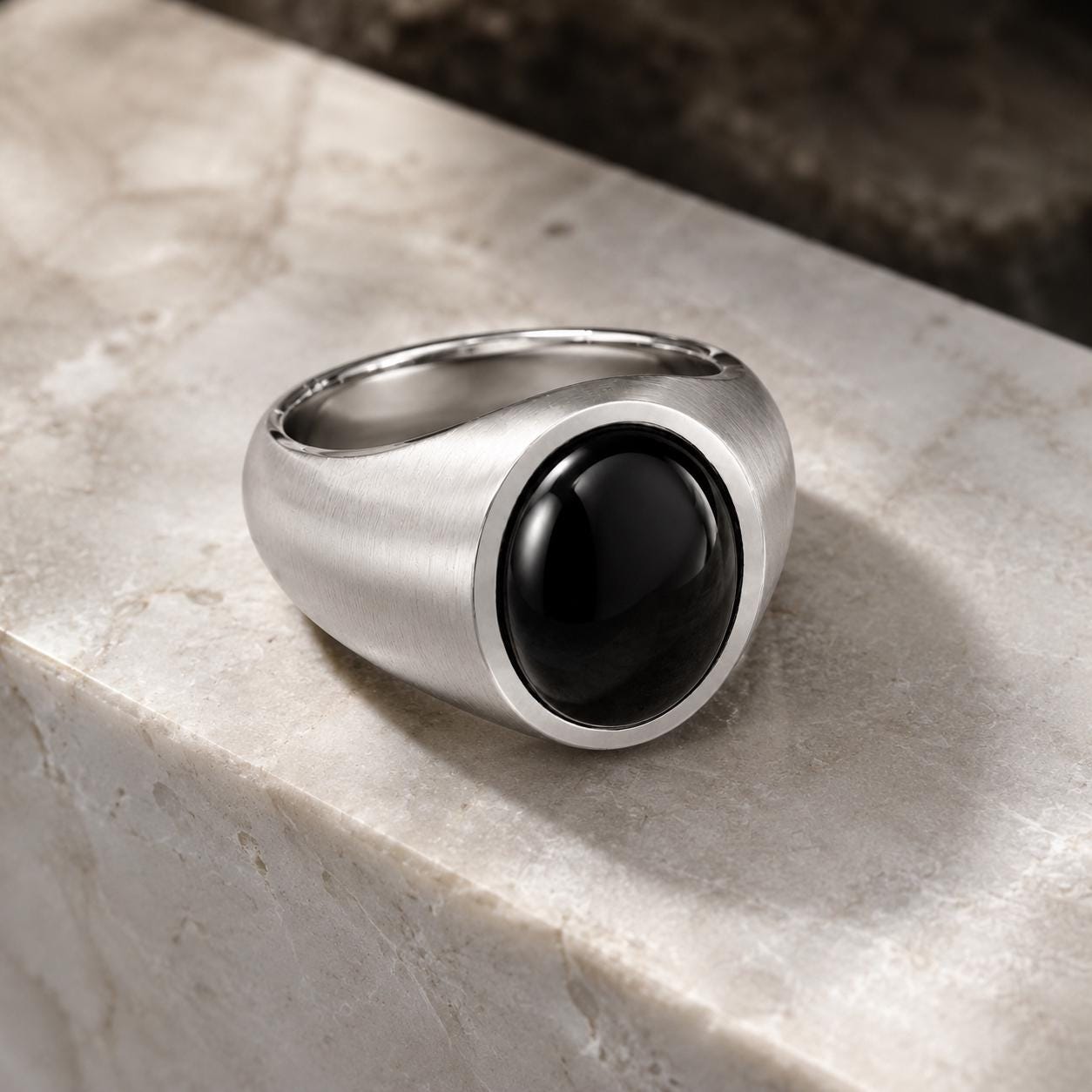 A silver ring with a black gemstone, possibly a diamond, is displayed on a marble surface.