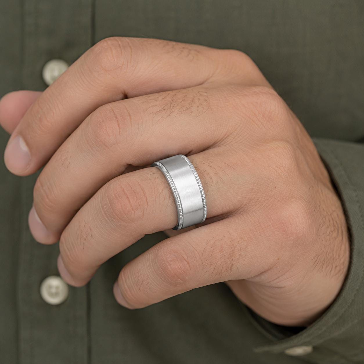 A close-up of a person's hand wearing a silver ring on the ring finger.