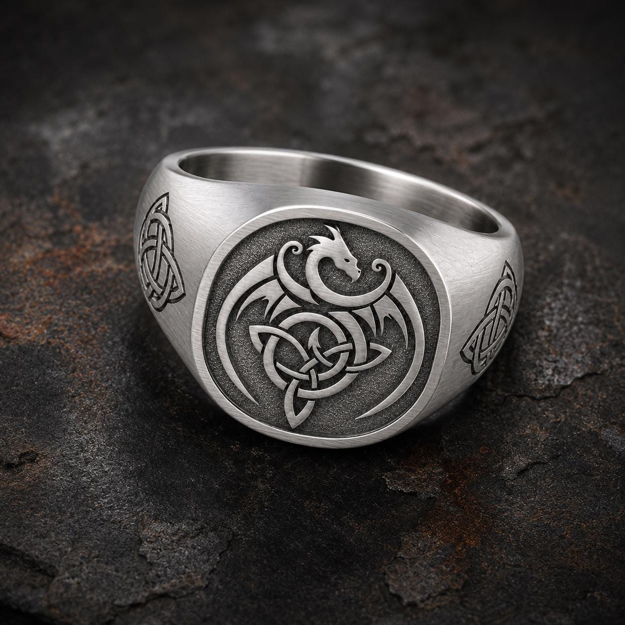 A silver ring with a dragon design and Celtic knot patterns.