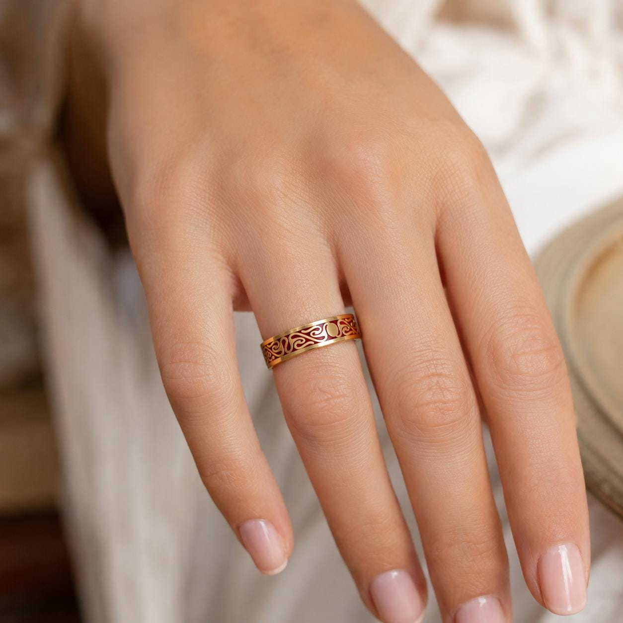 A close-up of a person's hand wearing a gold ring with an intricate design.