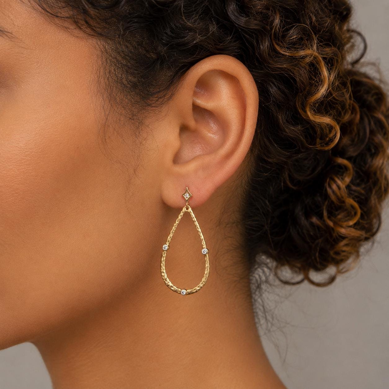 A close-up of a woman's ear wearing a gold earring with a diamond accent.