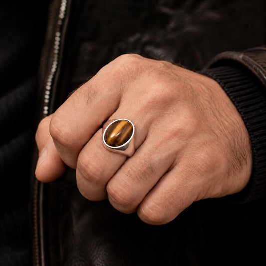 A close-up of a person's hand wearing a ring with a tiger's eye stone.