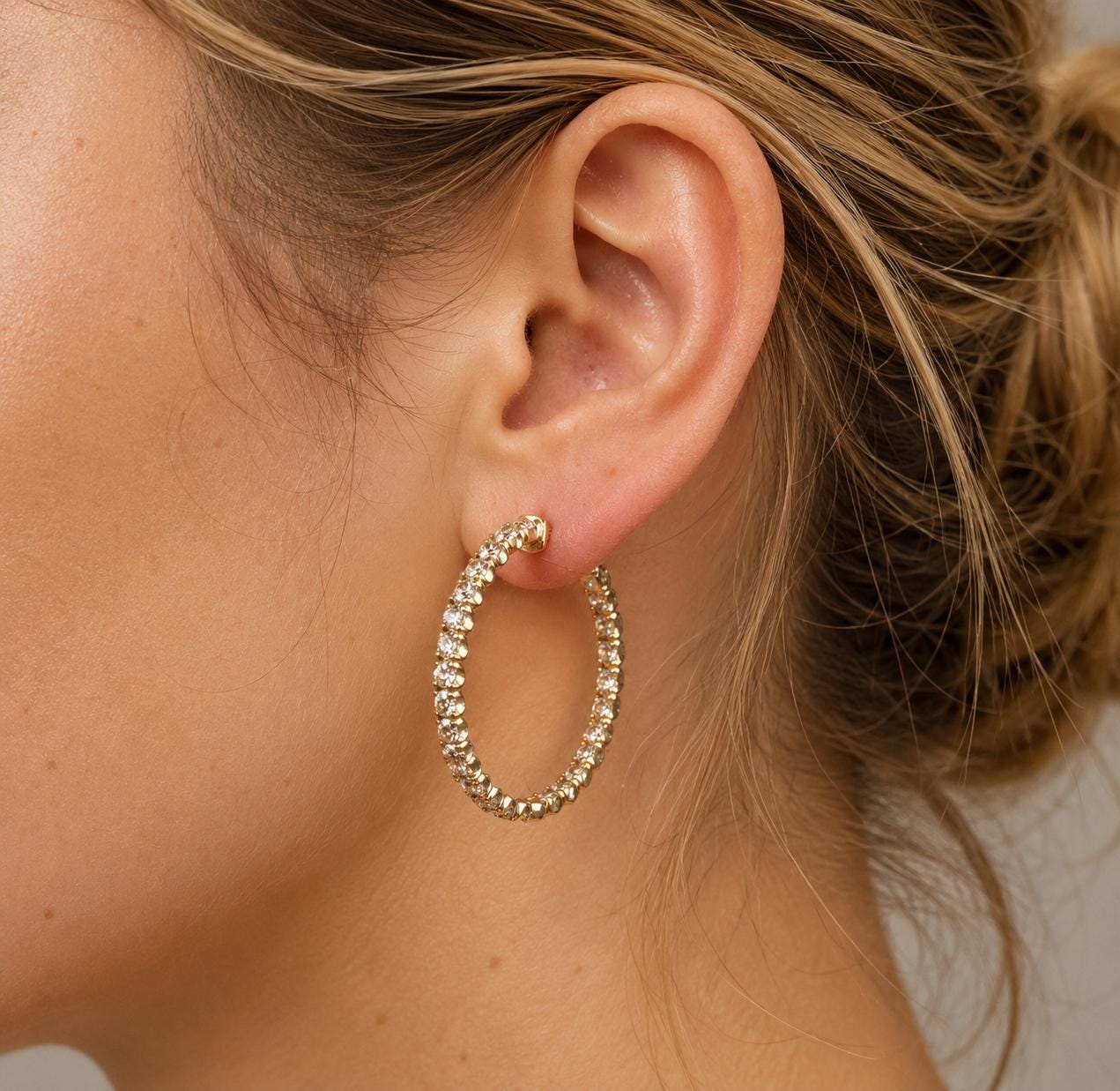 A close-up view of a woman's ear adorned with a gold hoop earring featuring a sparkling crystal design.