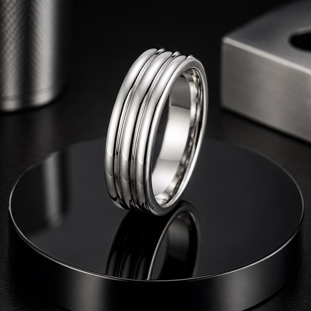 A silver ring with a unique design sits on a reflective black surface, surrounded by other metallic objects.