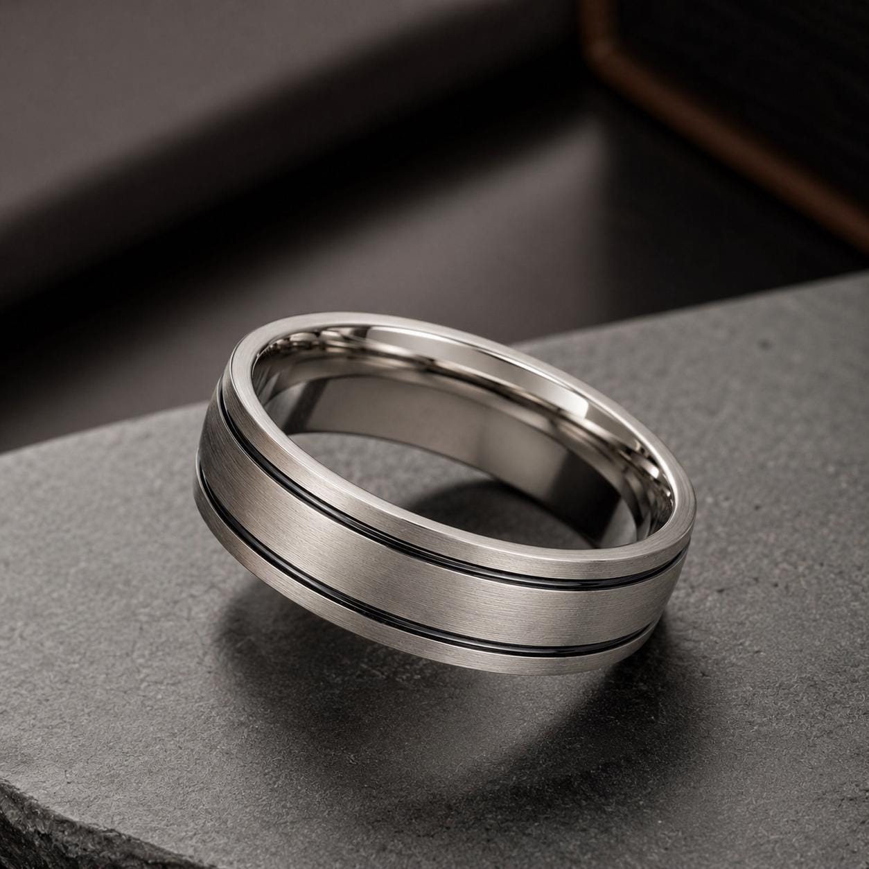 A silver ring with a horizontal band sits on a dark surface.