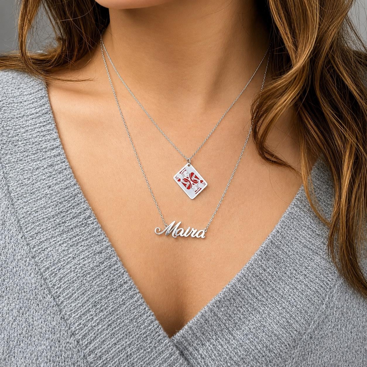 A woman wearing a gray sweater and a necklace with a pendant that says "Mara".