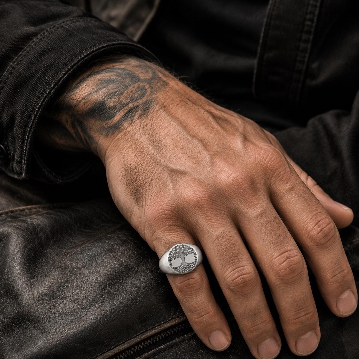 A close-up of a person's hand wearing a silver ring with a tree design on it.