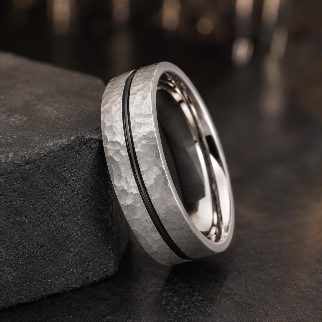 A silver ring with a black band is resting on a black surface, creating a striking contrast.