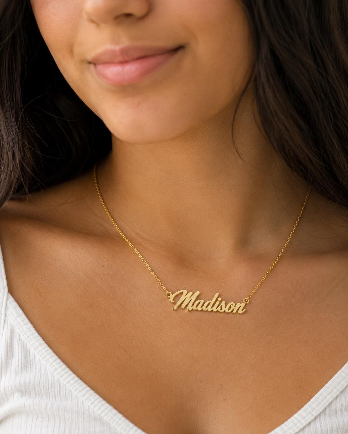 A close-up of a woman's neck and chest area wearing a gold necklace with the name "Madison" engraved on it.