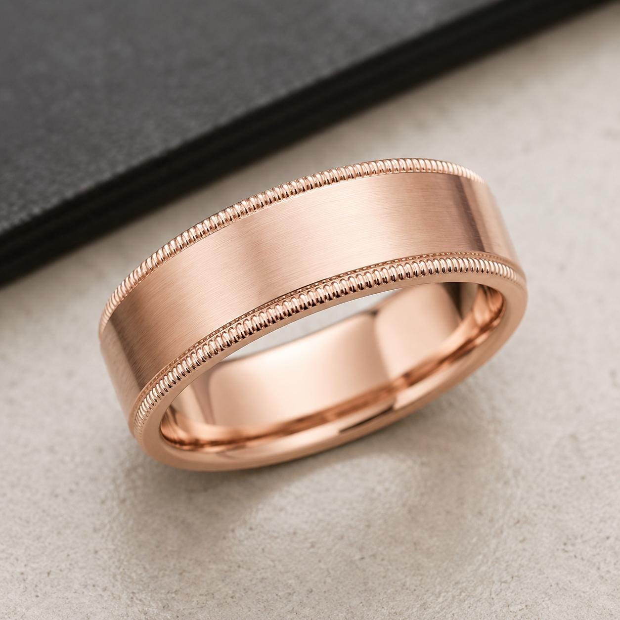 A rose gold ring with a textured band is displayed on a black surface.