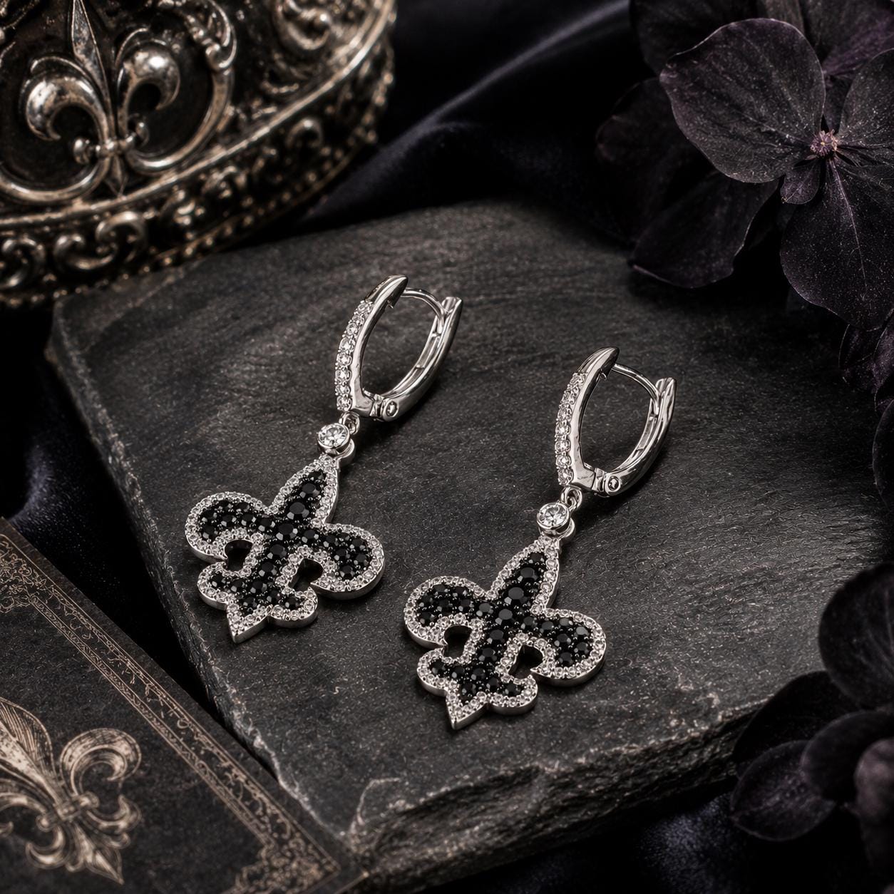 A pair of elegant earrings with black fleur-de-lis designs and sparkling gemstones, resting on a dark surface.