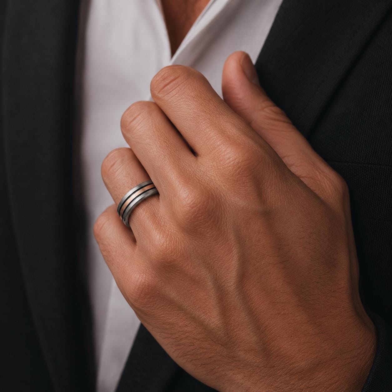 A close-up of a person's hand wearing a ring, with a black jacket visible in the background.