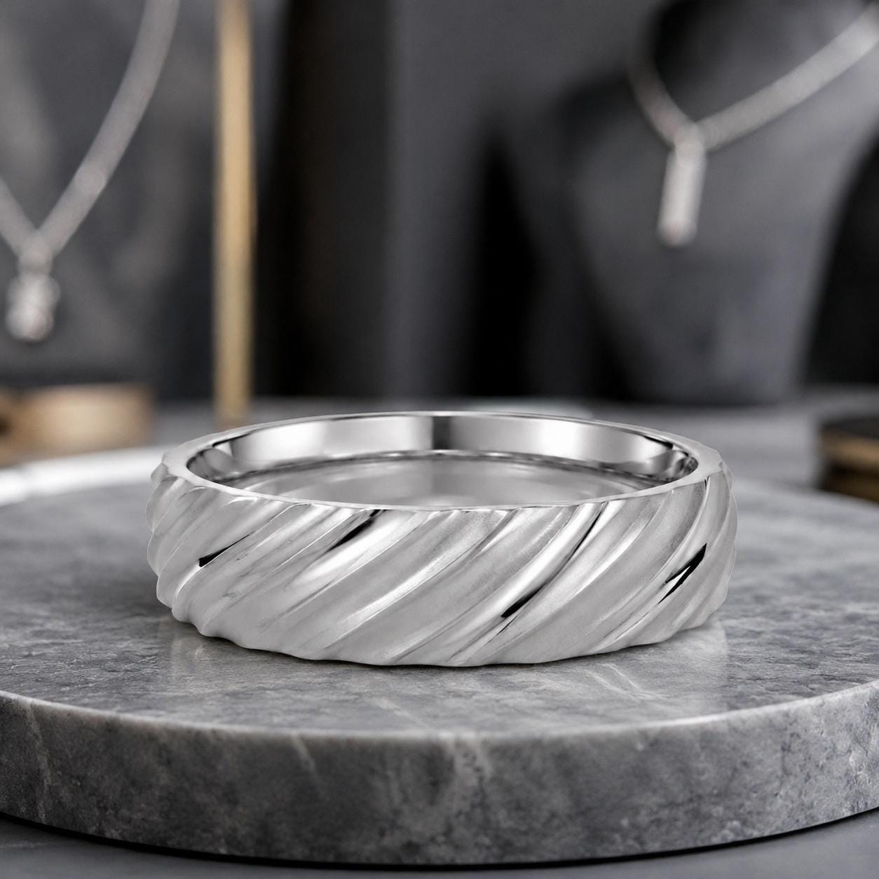 A silver ring with a twisted band sits on a gray marble surface, with other jewelry pieces visible in the background.