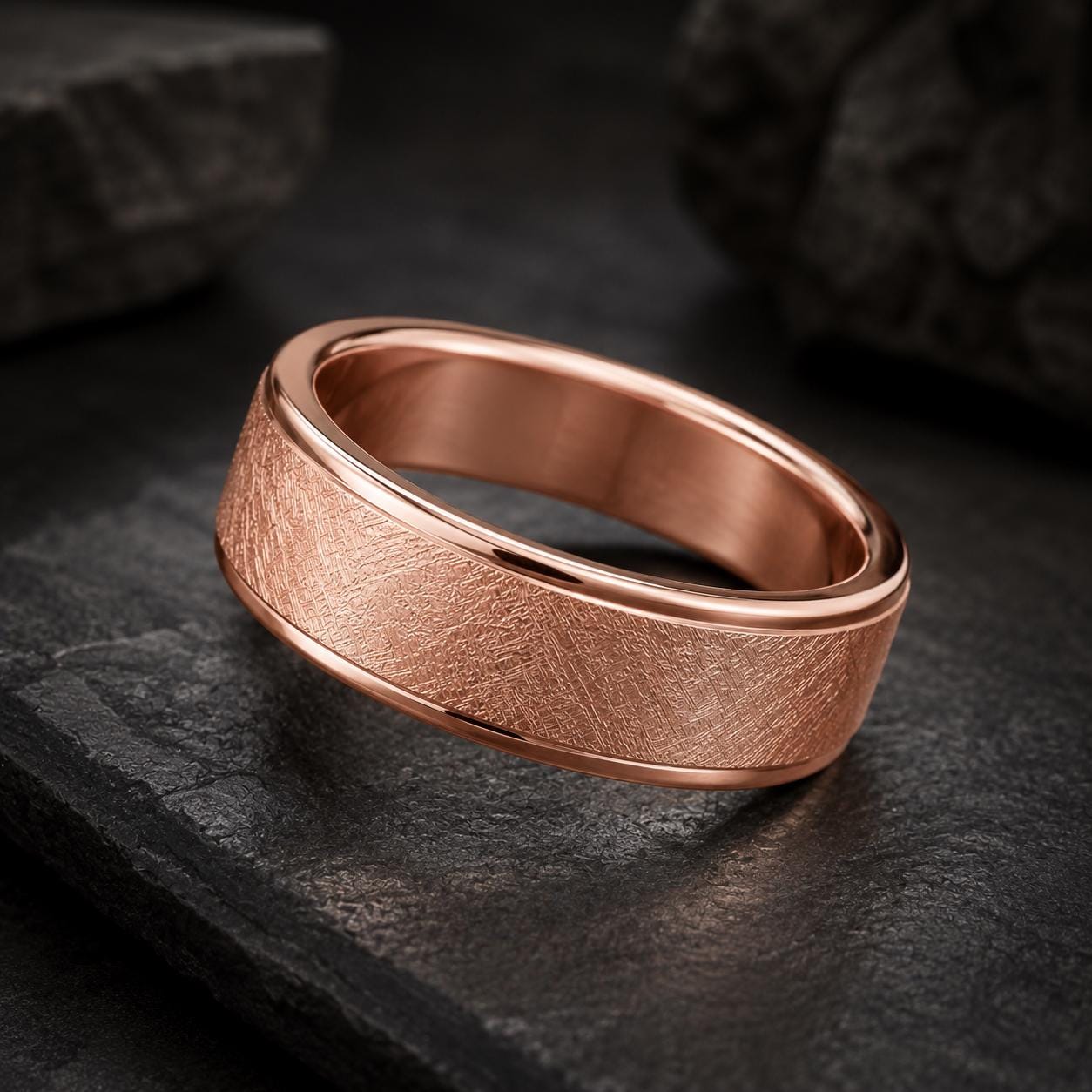 A copper-colored ring with a textured surface sits on a dark surface, surrounded by rocks.