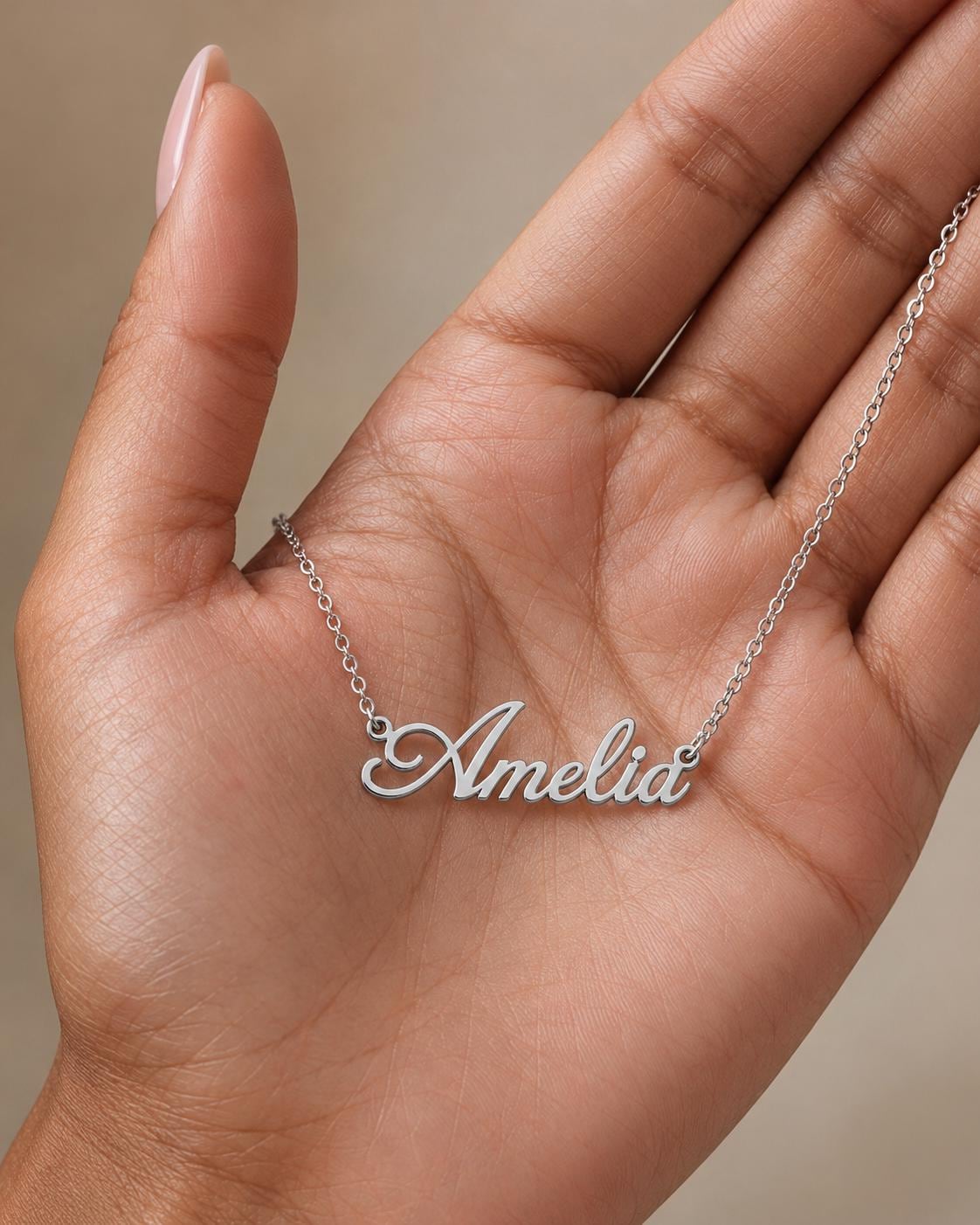 A hand holding a necklace with the name "Amelia" engraved on it.