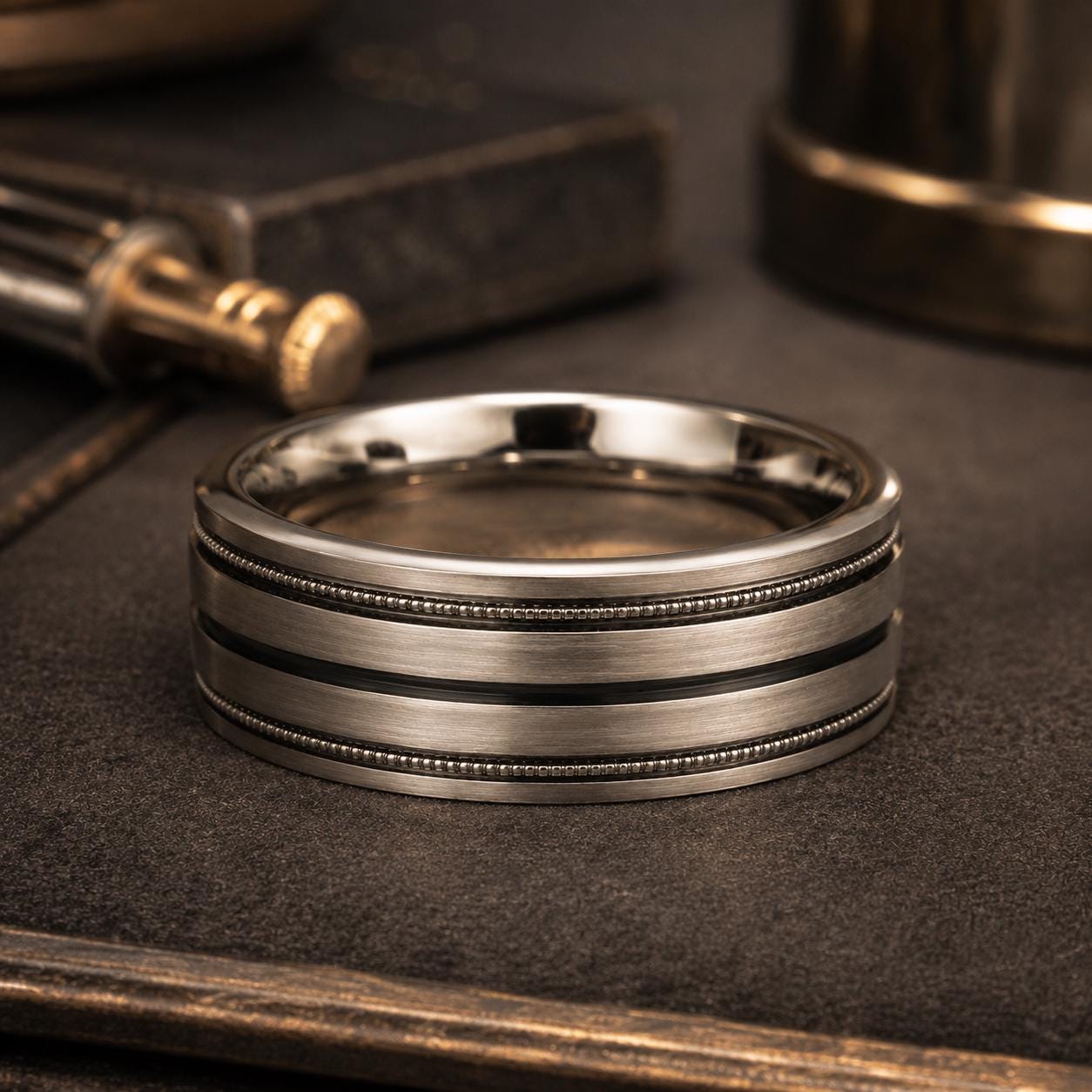 A silver ring with a striped band sits on a dark surface, surrounded by various objects such as a lighter and a book.